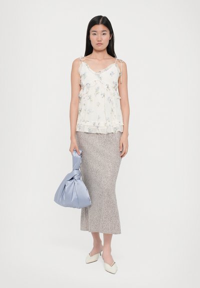 Camisola albă cu flori, cu detalii volănașe, fustă midi gri cu model, geantă ușor albastră cu nod, și pantofi mulo cu vârf ascuțit, de culoare crem.