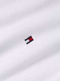 Vitt bomullstyg med mjuk textur, som har en liten, broderad logotyp i marinblått, rött och vitt. Subtil och minimalistisk design.