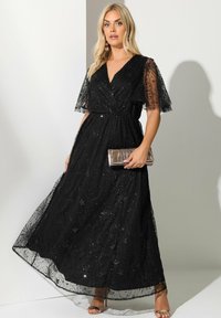 Mustapitsinen maksimekko, jossa on V-kaula-aukko, lyhyet liehuvat hihat ja monimutkainen paljettikoristelu. Yhdistetty metallinhohtoiseen clutch-laukkuun ja remmillisiin korkokenkiin.