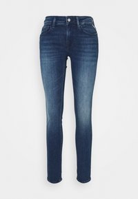 Jeans skinny de mezclilla azul con una cinturilla de altura media, diseño de cinco bolsillos y costuras en contraste, con una textura suave y un ligero desgastado.