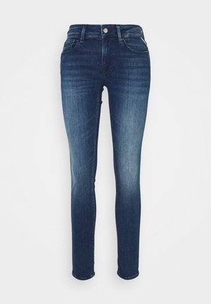 Jeans skinny de mezclilla azul con una cinturilla de altura media, diseño de cinco bolsillos y costuras en contraste, con una textura suave y un ligero desgastado.
