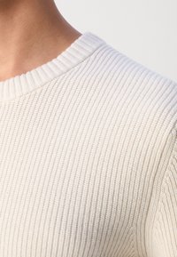 Hellbeiger gerippter Pullover mit rundem Ausschnitt und strukturiertem Strickmuster; zeichnet sich durch eine dezente Elastizität und eine weiche Haptik aus.