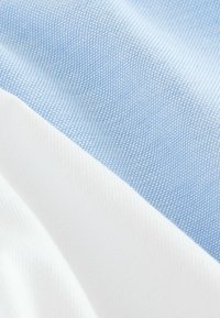 Heled sinine ja valge tekstureeritud kangas peene ruudustiku mustriga, mis näitab sujuvaid üleminekuid kahe värvi vahel.