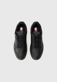 Zwarte sportieve schoenen met een gladleren bovenwerk, geperforeerde details, platte veters en merkinlegzolen met rode, witte en blauwe accenten.