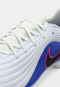 Λευκό ποδοσφαιρικό παπούτσι με επάνω μέρος από υφή δέρματος, γκρι κορδόνια και μπλε σόλα. Διαθέτει ροζ και μαύρο λογότυπο Nike swoosh.