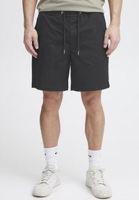 Shorts à cordon noirs en tissu léger, avec coutures latérales et coupe décontractée, portés avec des baskets blanches et des chaussettes montantes.