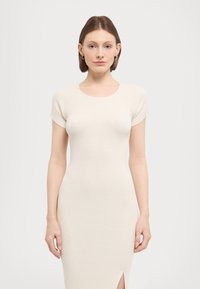 Jersey mekko off-white värissä, lyhyillä hihoilla, ribattua tekstuuria, istuva malli ja sivureikädetaali, joka luo virtaviivaisen siluetin.