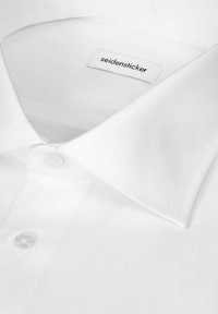Col de chemise blanche et boutons supérieurs avec une étiquette visible indiquant "seidensticker" à l'intérieur du col.