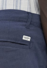 Παντελόνι από ύφασμα σκούρο μπλε ναυτικού χρώματος με υφή, διακοσμημένο με πίσω τσέπη και λευκή ετικέτα που γράφει «JACK & JONES EST. 1990».