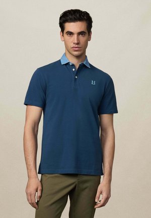 Mornarska polo majica s svijetloplavim ovratnikom, kratkim rukavima, izvezenim logotipom na prsima i glatkom pamučnom teksturom.