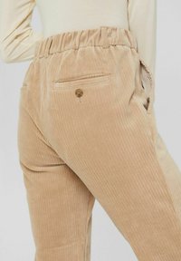 Beige kordflöjjebyxor med ribbad struktur, elastisk midja och bakfickor med knapplist.