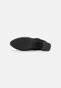 Zapato de ante negro con punta afilada, tacón bajo y suela de goma texturizada. Parte superior lisa sin patrones ni acentos visibles.