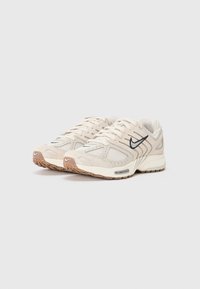 Beżowe sneakersy wykonane z siateczkowych i zamszowych materiałów, o zaokrąglonym nosku, z czarnymi akcentami logo oraz gumową podeszwą z brązowym wzorem bieżnika. Niskoprofilowy design.