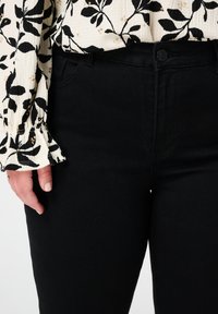 Zwarte spijkerbroek met hoge taille en standaardzakken, gedragen met een crèmekleurige blouse met lange mouwen en een zwart bladenpatroon.