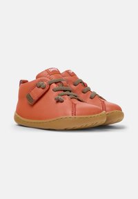 Pomarańczowe skórzane buty z zaokrąglonymi noskami, brązowymi sznurówkami i rzepem. Podeszwa jest miękka z teksturowanym gripem z gumy. Logo marki na języku.