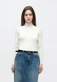 Biały prążkowany sweter z golfem w połączeniu z niebieską spódnicą jeansową. Spódnica ma przedni rozcięcie oraz czarny pasek ze złotą sprzączką.