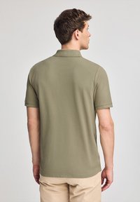 Olivgrön polo t-shirt med korta  ärmar, en krage och rak skärning, visad bakifrån mot en neutral bakgrund.