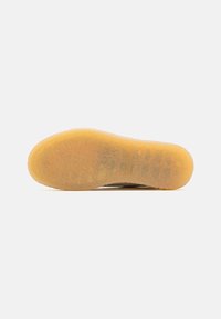 Semelle de chaussure avec semelle extérieure en gomme texturée, semi-translucide, présentée sur un fond blanc uni.