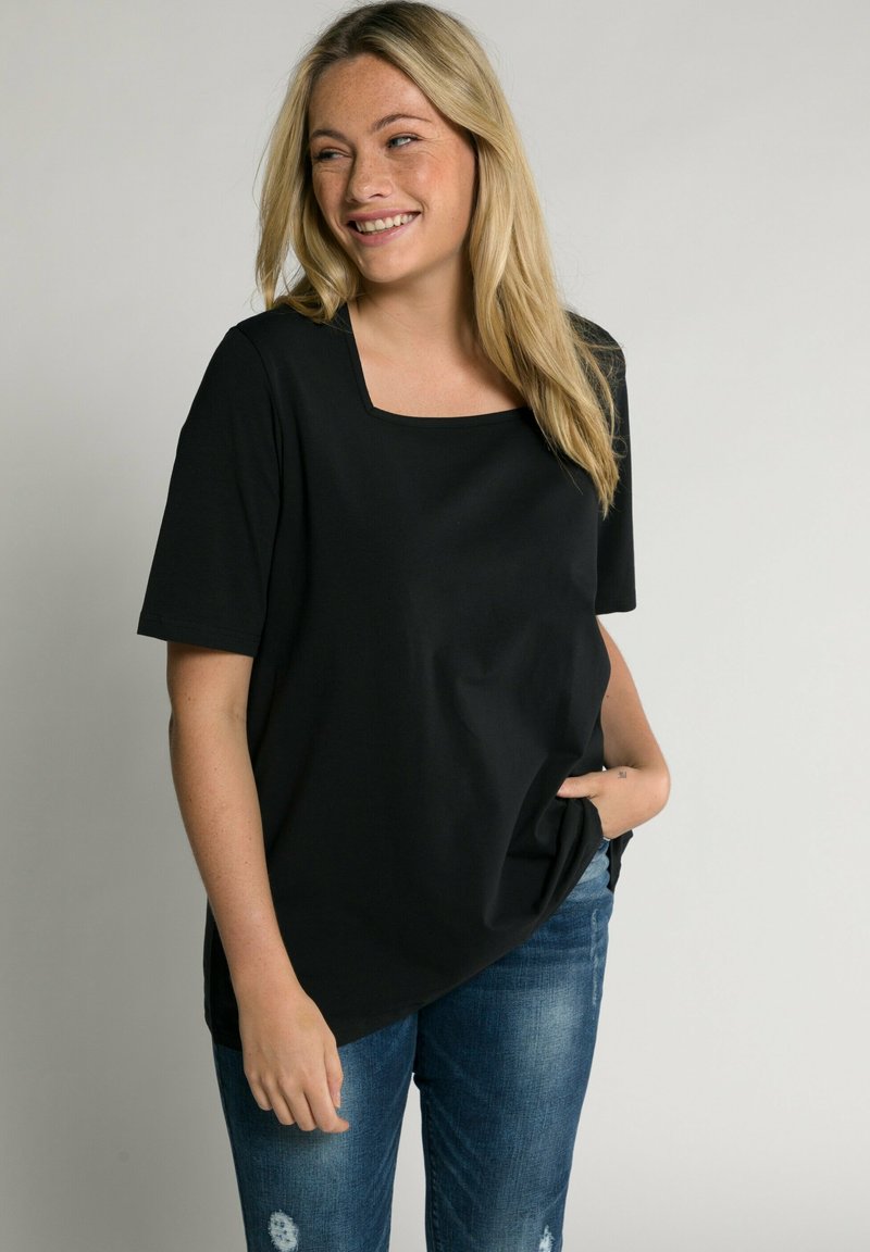 Top nero a maniche corte con scollo quadrato e vestibilità ampia, realizzato in tessuto morbido. Abbinato a jeans blu strappati, con le mani in tasca.