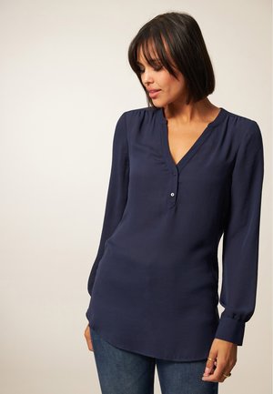 Marineblauwe blouse met lange mouwen, V-hals en knoopdetails, gemaakt van zachte stof, met geplooide schouders en een licht gebogen zoom.