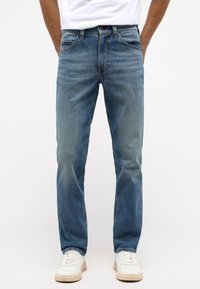 Ljusblå denimjeans med rakt ben, fem fickor, kontrasterande sömmar och en något blekt finish. Bärs med vita sneakers.