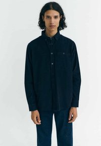 Donkerblauw overhemd met knopen, gemaakt van een gestructureerde stof, met een borstzak en lange mouwen. Gecombineerd met bijpassende donkere spijkerbroeken.