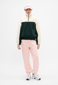 Pulover od flisa u tamnozelenoj i krem boji, sa zatvaračem do vrata, s džepovima. Mekane ružičaste trenirke, opuštenog kroja. Bijele i crne tenisice. Ružičasta kapa.