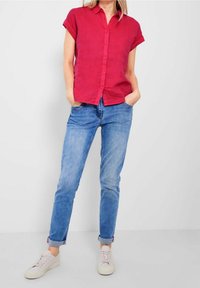 Rode linnen korte mouwen shirt met knopen aan de voorkant, gecombineerd met lichtblauwe spijkerbroek en beige sneakers, met een casual pasvorm.