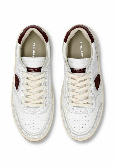 Hvide sneakers med tekstureret læder, burgunder detaljer, flade snørebånd og perforerede detaljer på tæerne. Mærkets navn er synligt på tungen.