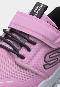 Ροζ αθλητικό παπούτσι με μαύρα ελαστικά κορδόνια, ιμάντα με βέλκρο και μαύρη ετικέτα που αναγράφει "Skechers 1992".