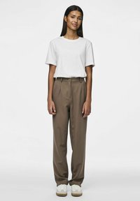 Weißes Baumwoll-T-Shirt, entspannte Passform, kombiniert mit hochgeschnittenen, braunen maßgeschneiderten Hosen und weißen Sneakern mit braunen Akzenten. Einfaches Design.