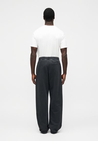 Lazán illeszkedő fekete melegítőnadrág rugalmas derékpánttal és oldalzsebbel, egyszerű fehér pólóval párosítva, hátulnézetből.