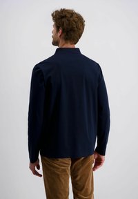 Marineblauw polo t-shirt met lange mouwen en kraag, met een gladde textuur en een rechte snit, gecombineerd met lichtbruine ribfluwelen broek.