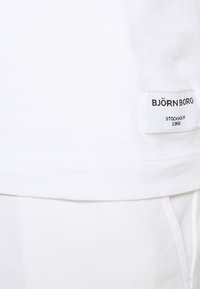 White t-shirt with a soft texture, featuring a BJÖRN BORG label stitched at the bottom. Simple design, an understated style.