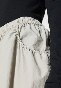 Black long-sleeve top with a cream elastic-waisted skirt featuring gathered fabric and a side pocket, displaying a smooth texture.