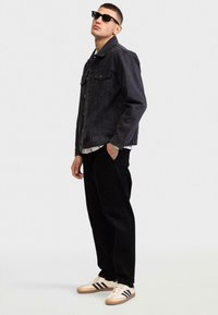 Zwarte spijkerjack met vo pockets, gedragen over een wit geruit shirt. Zwarte relax-pants en beige sneakers met zwarte strepen.