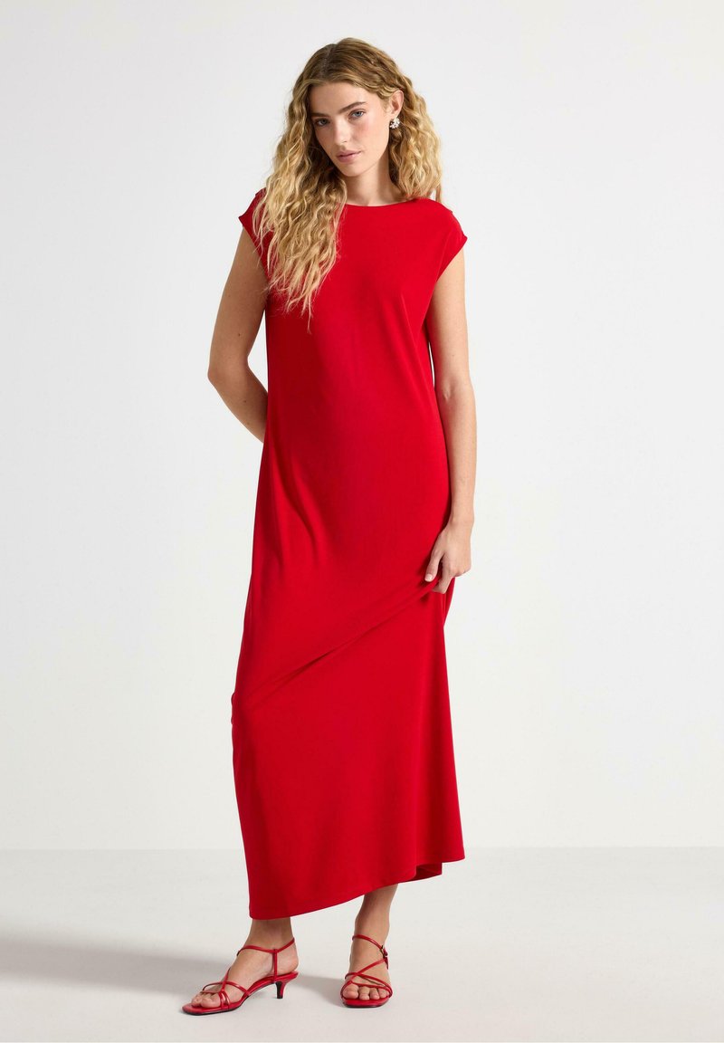 Maxi dress rossa realizzata in tessuto morbido, con scollatura rotonda, maniche corte e una silhouette fluente. Abbinata a sandali rossi con cinturino.