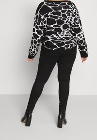 Suéter grande de patrón en blanco y negro con mangas anchas, combinado con pantalones negros ajustados y botas de tacón negras hasta el tobillo.