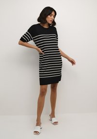 Rochie tricotată cu dungi alb-negru, cu mâneci scurte, gât rotund, buzunare laterale și o croială lejeră, ajungând până la mijlocul coapsei.