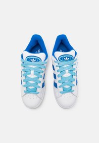 Baskets blanches avec des accents bleus, présentant trois rayures bleues, des lacets bleus et un logo circulaire bleu sur la languette. Texture en cuir et tissu lisse.