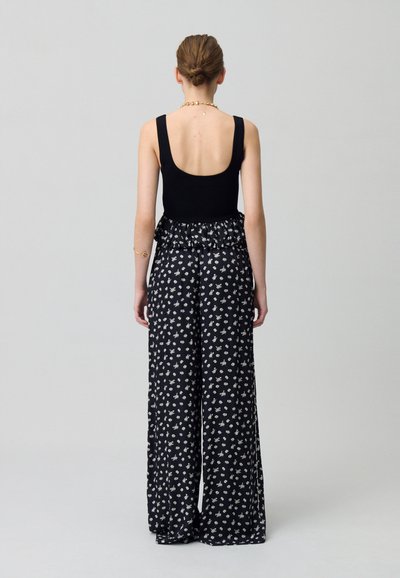 Top nero senza maniche con schiena bassa abbinato a pantaloni a gamba larga caratterizzati da un motivo floreale bianco e nero e una vita arricciata.