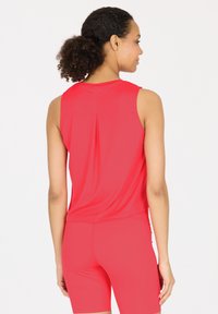 Rode mouwloze sporttop met een rugplooitje, gemaakt van gladde, rekbare stof; gecombineerd met bijpassende rode shorts.