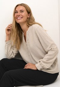 Langärmlige, knöpfbare Bluse in Beige mit dezenten weißen Streifen. Mit Rundhalsausschnitt und gerafften Bündchen. Glatte Textur.