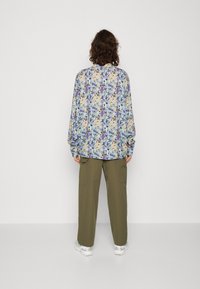 Blusa multicolor con un estampado abstracto en azul, púrpura y beige, con mangas largas y un corte relajado, combinada con pantalones cargo oliva.