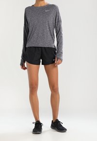 Haut de sport gris à manches longues avec un col arrondi et un logo Nike, assorti à un short noir et des chaussures de sport noires.
