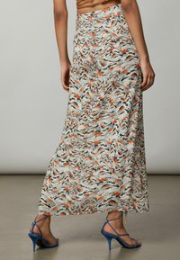 Falda larga de tela ligera, con un patrón ondulado multicolor en tonos naranja, negro y crema. Incluye una abertura lateral.