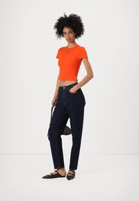 Kirjava oranssi crop-top, ribbed-kankainen, yhdistettynä tummansinisiin korkea vyötäröisiin farkkuihin, litteisiin mustiin kenkiin ja pieneen mustaan käsilaukkuun.
