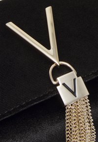 Black fabric clutch featuring a prominent gold V-shaped hardware accent, connected by a ring to a gold chain tassel detail.