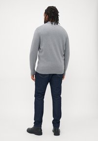 Grå strikkegenser med ribbestrikkede mansjetter og nederkant, brukt med mørkeblå jeans og svarte støvler, vist fra baksiden mot en hvit bakgrunn.