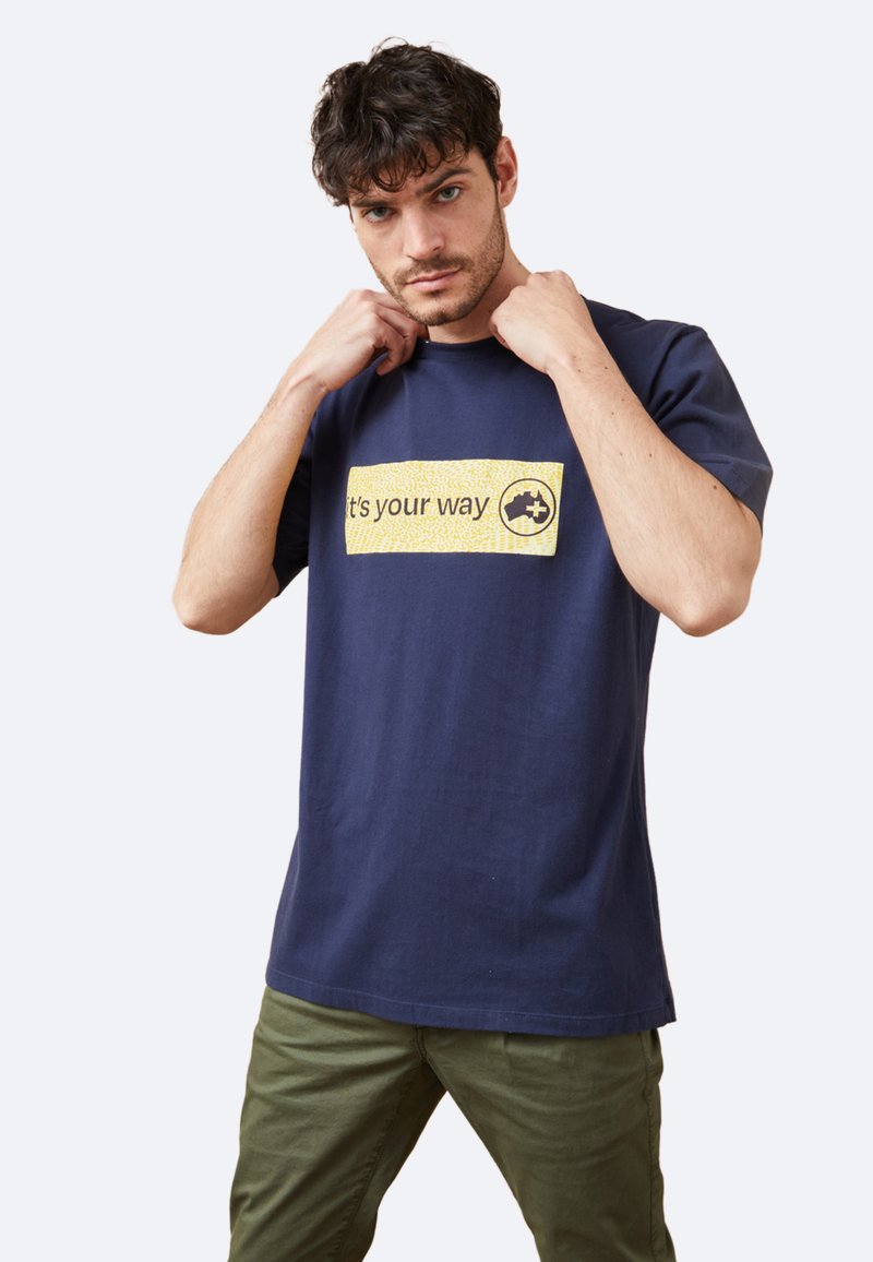 Camiseta de algodón azul marino de manga corta con un rectángulo gráfico amarillo que dice "es tu camino" y un logo. Textura suave.